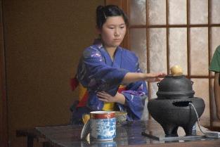 青色の浴衣を着て風炉に伸ばした手の方の裾を持っている様子の、お茶を立てている女性の写真