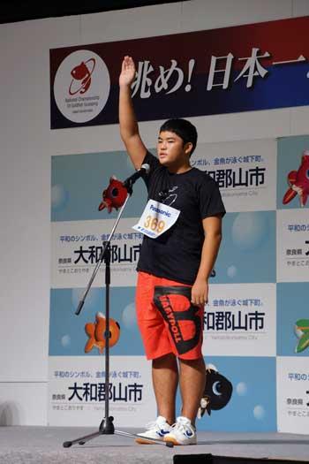黒色のシャツと赤いパンツを履いた男の子が選手宣誓している写真