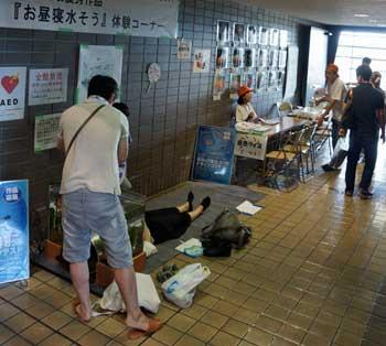 「お昼寝水そう」体験コーナーで床に敷かれたシートの上で横になっている女性と、その前に立つ白色のシャツを着た男性の写真