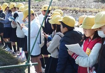 黄色の帽子をかぶって並んで資料を見たりメモをしている子供たちの写真