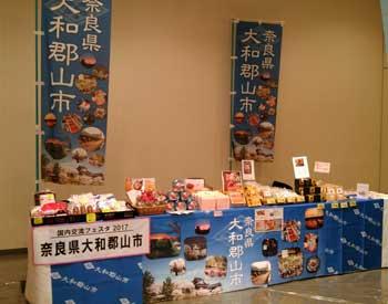 青字に白い文字で奈良県大和郡山市と書かれたのぼり2本と物産品が並べられている長テーブルの写真