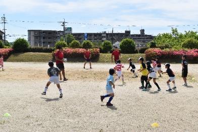 近鉄ライナーズのラグビー選手と子どもたちが広場でラグビーボールを追いかける写真