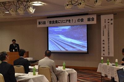 第5回「奈良県にリニアを！」の会」と書かれた横断幕とプロジェクターの映像を使って講演している写真