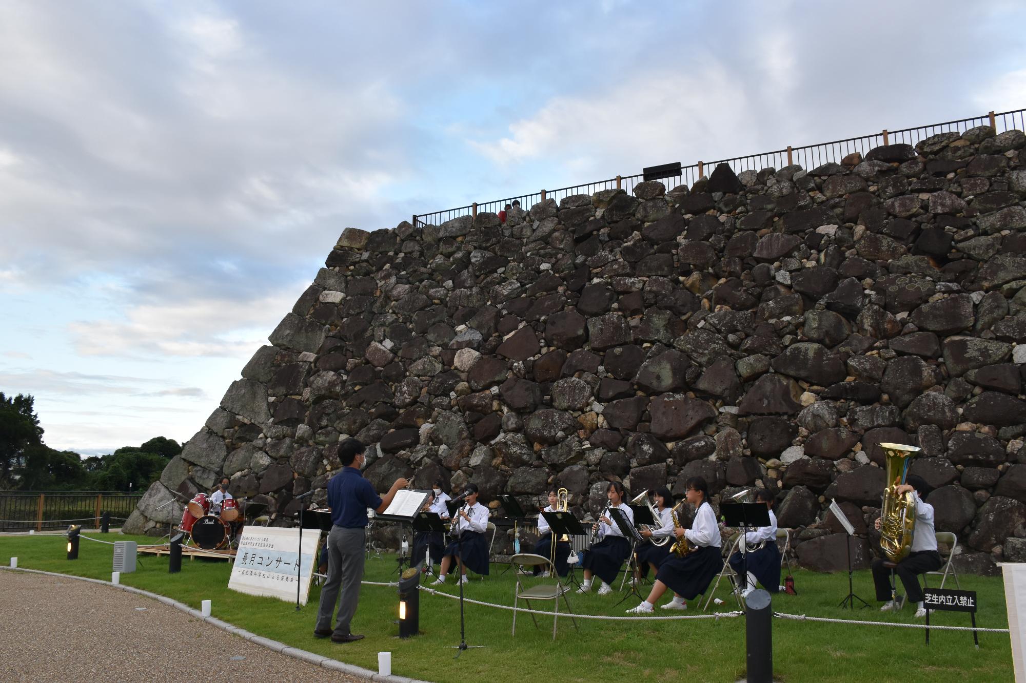 天守台の石垣の前で演奏する吹奏楽部の生徒達10名