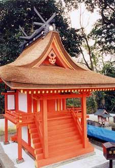 木々を背景にした、檜皮葺の屋根を持つ朱塗りの春日神社本殿の写真