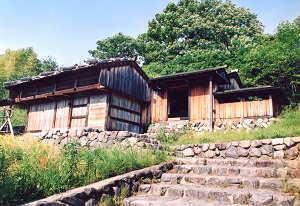 木々と青空を背景に、石段の奥に立つ旧木村家住宅の写真