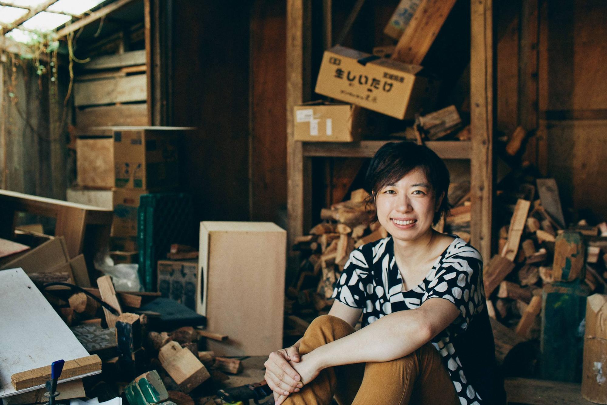 講師の渡辺享子さんが木材加工場で座っている写真