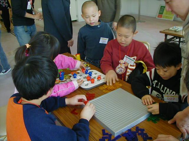 机の上に置かれたゲーム玩具で遊ぶ子供達の写真