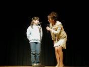 マイクスタンドを前に立つ小さな女の子と、マイクを手にかがんで話しかける女性の写真