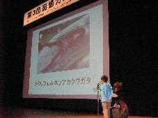 クワガタの写真が映し出されたスクリーンを背に、暗唱発表をしている男の子の写真