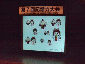 複数のキャラクターイラストが映し出された、舞台上のスクリーンの写真