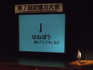 漢字の部首が表示されたスクリーンと、舞台上で発表をしている子供の写真
