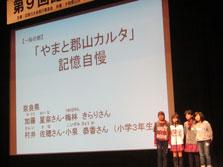 舞台上でカルタ記憶自慢の発表をしている4人の女の子のグループの写真