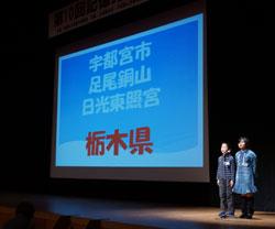 栃木県宇都宮市足尾銅山日光東照宮と写されたスクリーンの前で2人が立っている写真