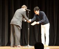 スーツを着た男性が記憶力日本選手権総合チャンピオンに賞を渡している写真