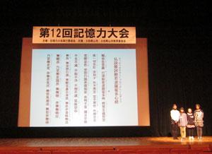 スクリーンに映し出された文章を背に、暗唱発表をしている4人組のグループの写真