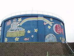 青い外壁に虹や星、地球などのイラストが描かれた、円筒形の受水タンクの写真