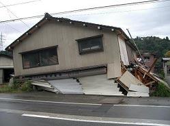 一階が潰れて倒壊している三角屋根の一軒家の写真