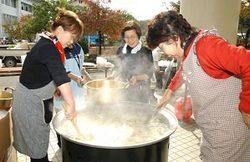 屋外で、大きな鍋を囲み炊き出し料理を作っている女性たちの写真