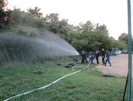 グラウンドで放水訓練をする消防団員たちの写真