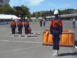 屋外で整列する消防団員とオレンジ色の箱の写真