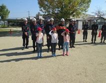 屋外で敬礼する子供たちと消防団員の写真