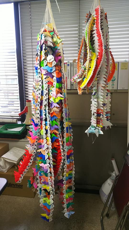様々な色の折り紙で作られた金魚の束が2本吊るされている写真