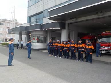 消防署前で整列する消防団員たちと敬礼する消防団員の写真
