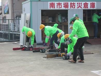 防災倉庫前で作業する緑色の上着を着た人たちの写真