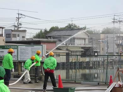 屋外で放水訓練をする緑色の上着を着た人たちの写真