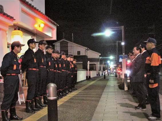 夜間に消防署前で整列する消防団員を斜めから撮った写真