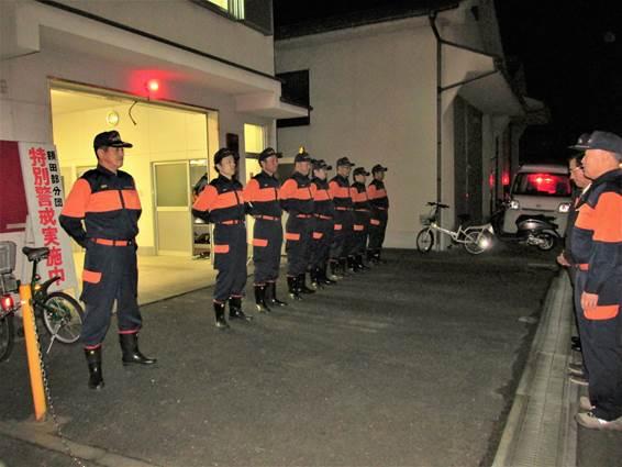 夜間に消防署前で整列する消防団員の写真