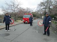 道路で警備する消防団員と消防車の写真