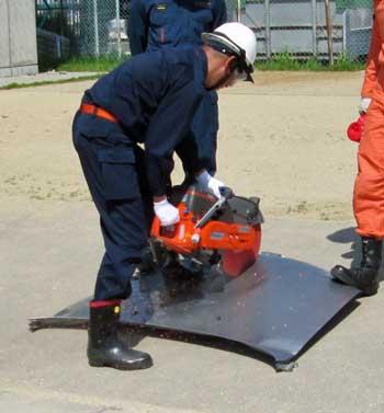 屋外でエンジンカッターを使用した訓練をする消防団員の写真